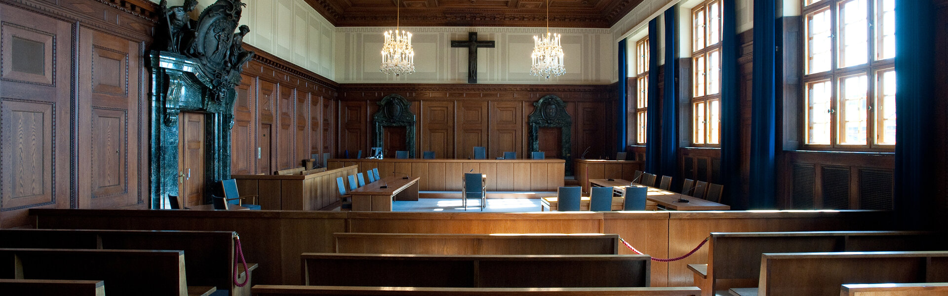 Blick in den historischen Saal 600 des Memoriums Nürnberger Prozesse mit Holzvertäfelung, Kronleuchtern und Holzbänken.