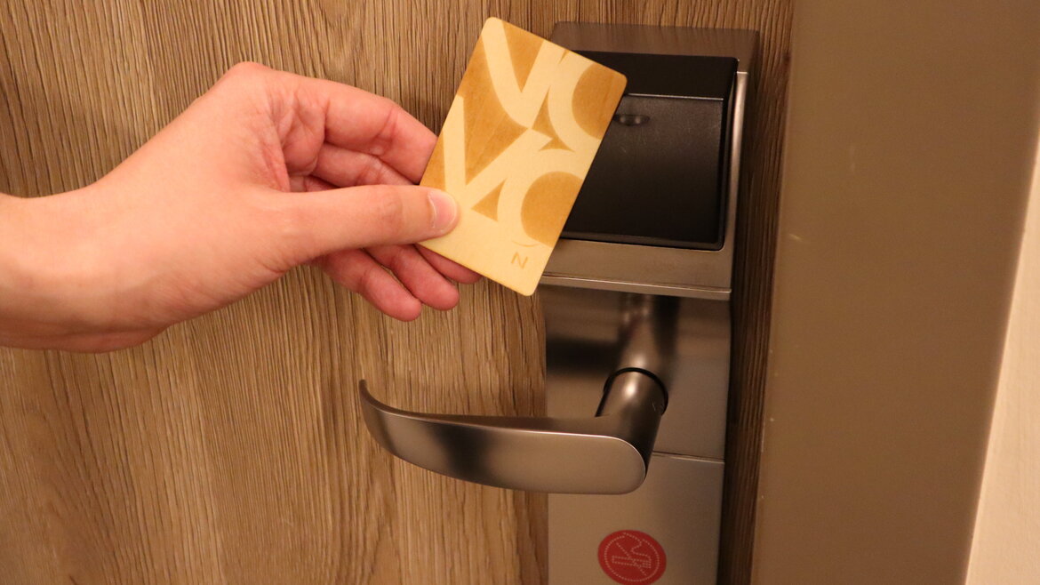 Hand hält eine gelbe Zimmerkarte vor einen elektronischen Türgriff an einer Holztür