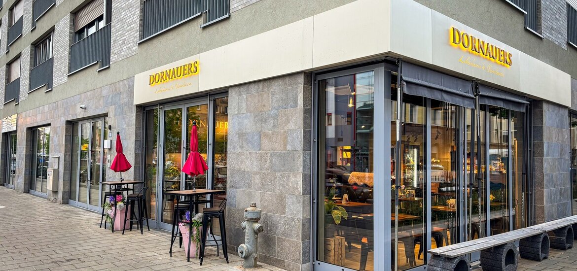 Gebäudeansicht und Eingang zu DORNAUERS in einem neugebauten Wohn- und Geschäftshaus. Moderne optik in grau gehalten. Große Fenster, die einen Blick in den Verkaufsraum bieten.