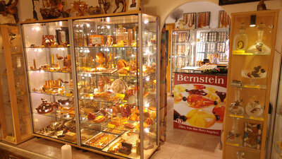 Vitrinen im Bernstein Museum Nürnberg mit zahlreichen Bernsteinobjekten wie Schmuck und Skulpturen, daneben ein Plakat mit der Aufschrift 'Bernstein Alles, was das Herz begehrt'