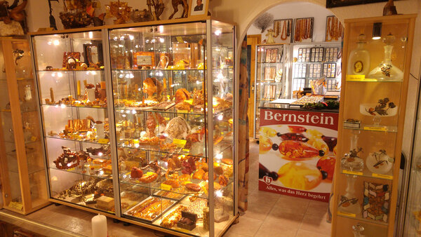 Vitrinen im Bernstein Museum Nürnberg mit zahlreichen Bernsteinobjekten wie Schmuck und Skulpturen, daneben ein Plakat mit der Aufschrift 'Bernstein Alles, was das Herz begehrt'