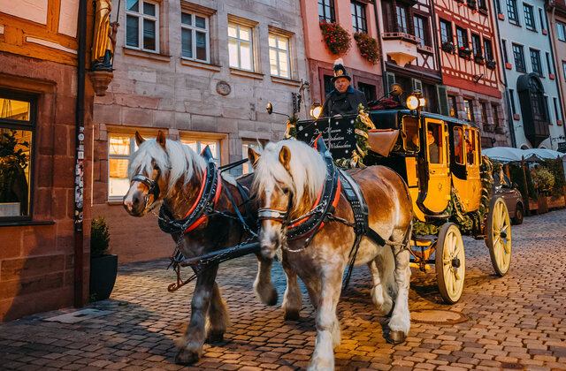 Gelbe Postkutsche mit zwei Pferden vor Fachwerkhäusern in der Weißgerbergasse, Nürnberg, bei Dämmerung.