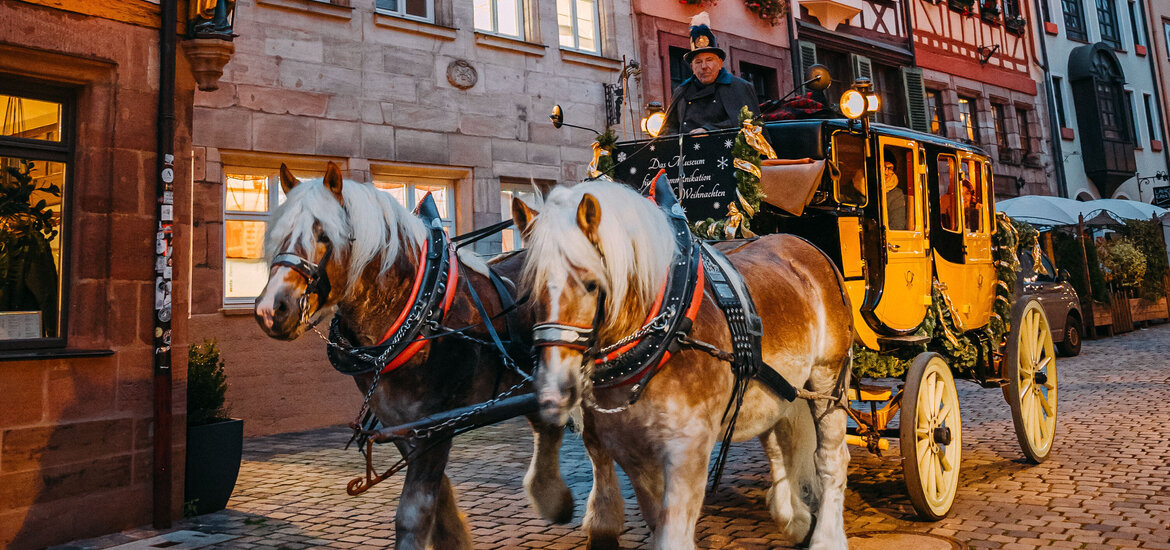 Gelbe Postkutsche mit zwei Pferden vor Fachwerkhäusern in der Weißgerbergasse, Nürnberg, bei Dämmerung.