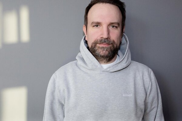 Ein Porträt von Matt Schwarz, der in einem grauen Kapuzenpullover vor einer schlichten grauen Wand steht.