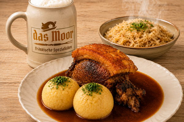 Schäufele mit knuspriger Kruste, zwei Klößen in dunkler Soße, daneben ein Teller Sauerkraut und ein Steinkrug mit Schaumkrone und dem Schriftzug 'das Moor Fränkische Spezialitäten'.