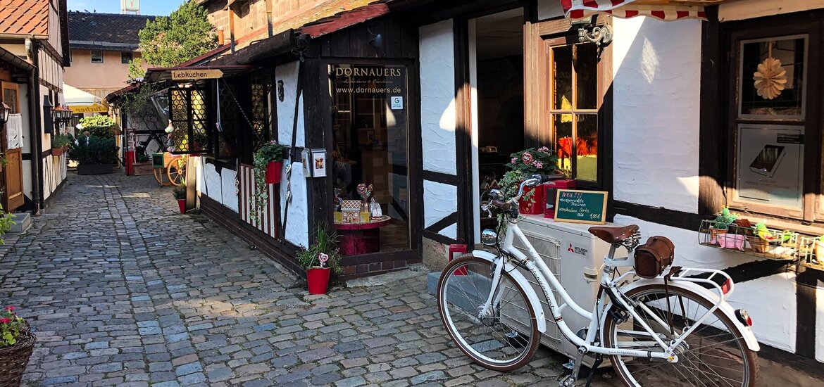 Eingangstür im kleinen FAchwerkhaus von DORNAUERS im Handwerkerhof. Im Vordergrund ein weißes Fahrrad und der Weg mit Pflastersteinen.