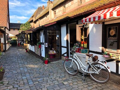 Eingangstür im kleinen FAchwerkhaus von DORNAUERS im Handwerkerhof. Im Vordergrund ein weißes Fahrrad und der Weg mit Pflastersteinen.