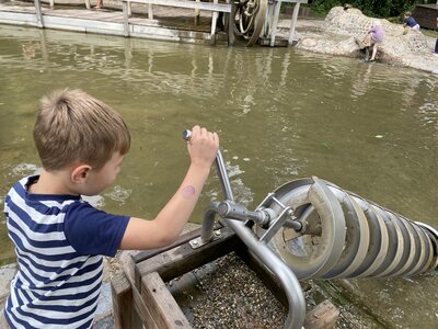 Kind bedient am Erfahrungsfeld Nürnberg eine Wasserspielanlage mit einer großen spiralförmigen Schnecke aus Metall über einem Wasserbecken