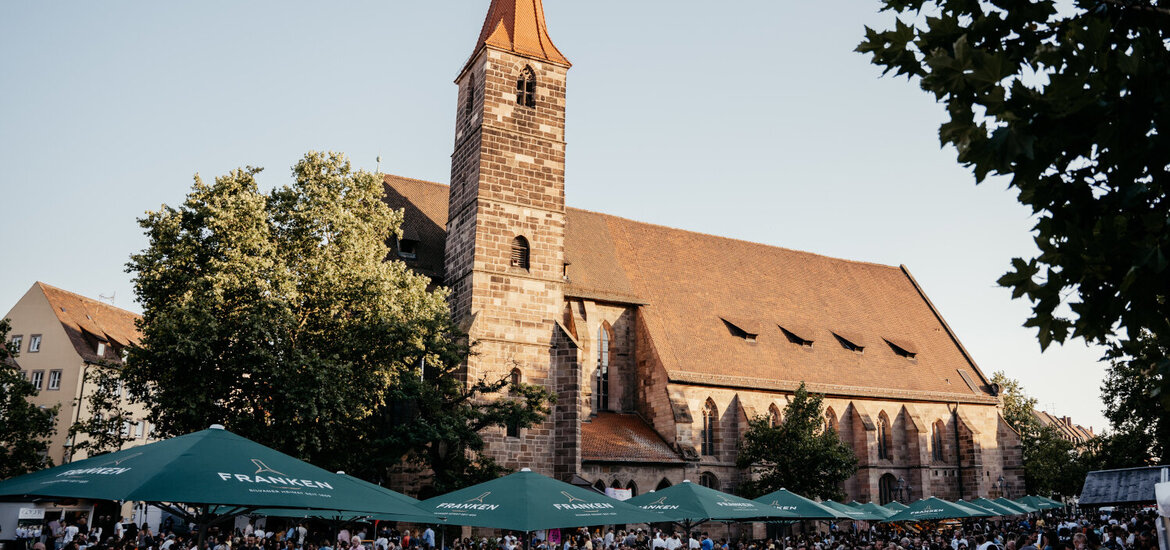 Menschenmenge unter grünen Sonnenschirmen vor der Jakobskirche beim Weinfest in Nürnberg bei Tageslicht