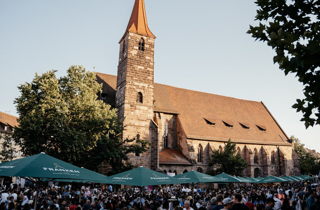 Menschenmenge unter grünen Sonnenschirmen vor der Jakobskirche beim Weinfest in Nürnberg bei Tageslicht