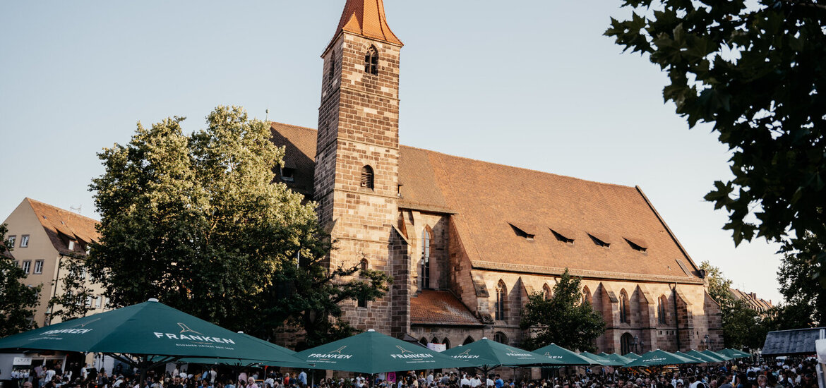 Menschenmenge unter grünen Sonnenschirmen vor der Jakobskirche beim Weinfest in Nürnberg bei Tageslicht