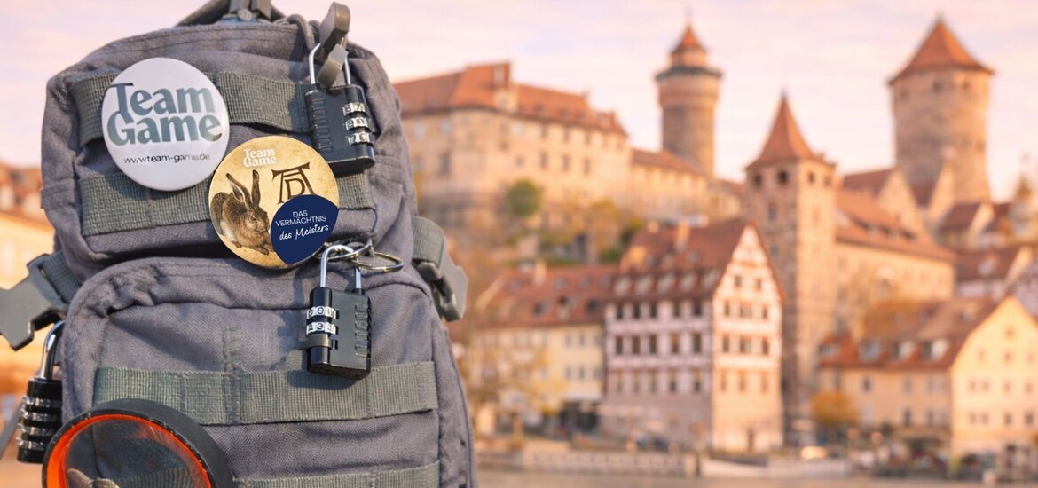 Grauer Rucksack von Team Game mit mehreren Vorhängeschlössern, zwei runden Ansteckbuttons und einer Lupe vor einer Kulisse mit dem Fluss Pegnitz, historischen Gebäuden und der Kaiserburg..