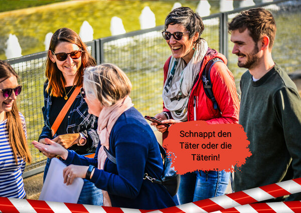 Fünf lachende Erwachsene stehen im Freien vor einem Zaun, eine Person hält ein Klemmbrett, im Vordergrund ein rot-weißes Absperrband und eine Sprechblase mit dem Text 'Schnappt den Täter oder die Täterin!'