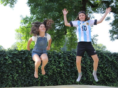 Zwei Kinder springen auf einem Wasserkissen im Erfahrungsfeld Nürnberg vor einer Hecke, eines trägt eine Latzhose, das andere ein Fußballtrikot.