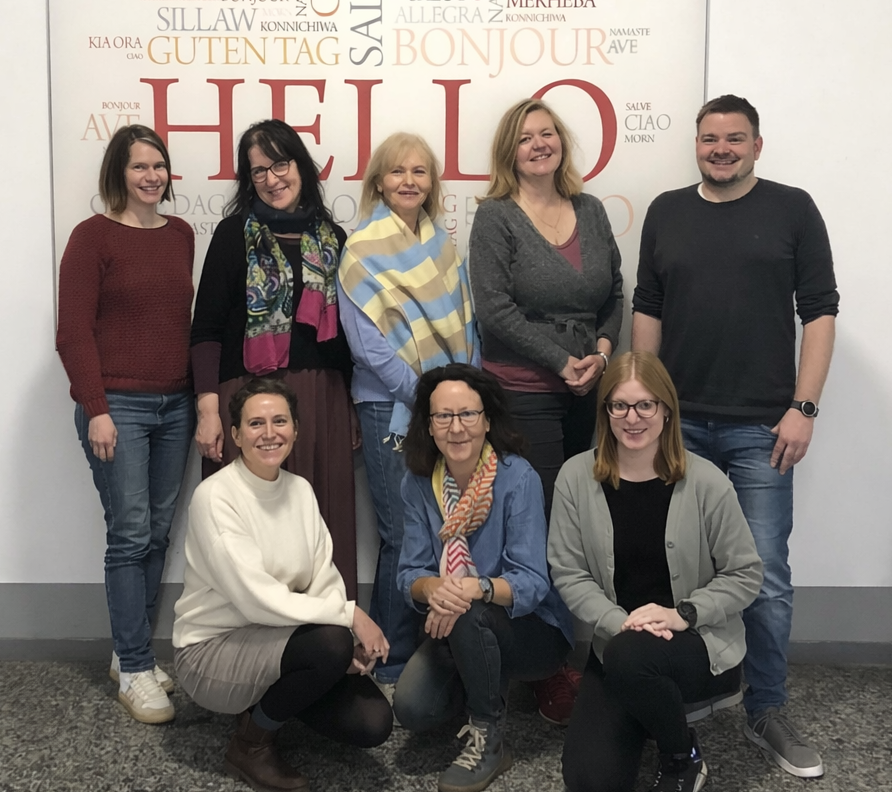 Gruppenfoto des Teams der Tourist Information Nürnberg vor einer Wand mit dem Wort "HELLO" und verschiedenen Begrüßungen in mehreren Sprachen