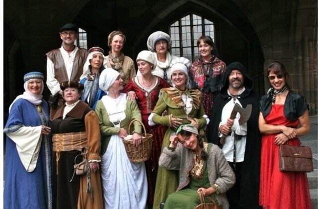 Ein Gästeführer in einem rosa-weiß karierten Hemd steht vor einer Touristengruppe an der Pegnitz. Er trägt ein Namensschild um den Hals und hält eine schwarze Mappe mit der Aufschrift „GESCHICHTE FÜR ALLE e.V. – Institut für Regionalgeschichte“ im Arm.