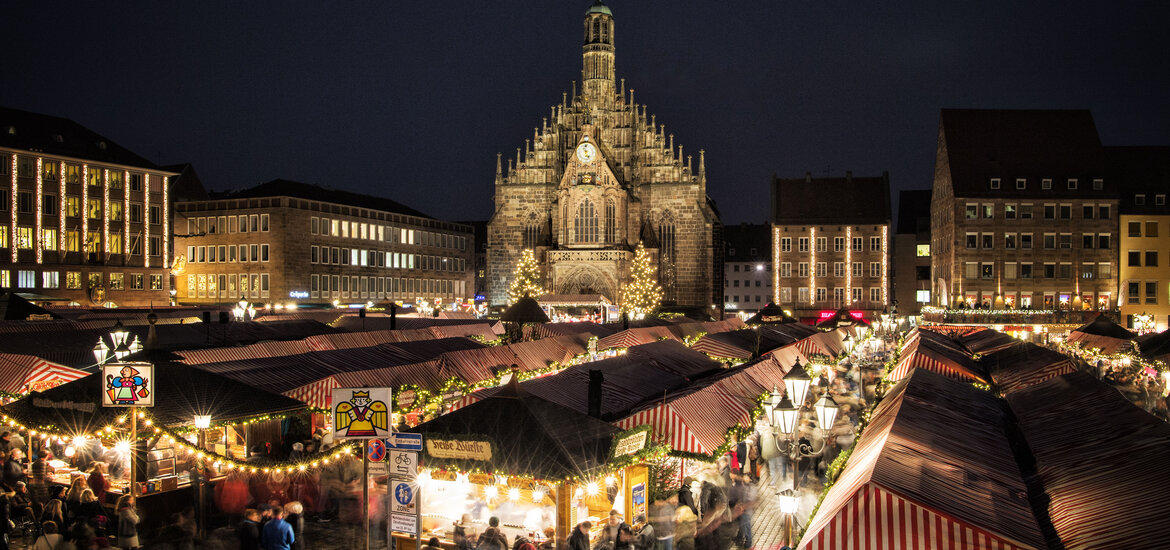 Nürnberger Christkindlesmarkt mit beleuchteten Marktständen und der Frauenkirche im Hintergrund bei Nacht.