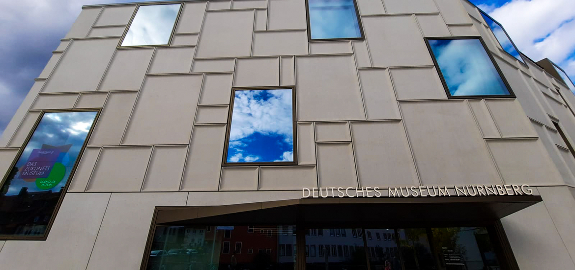 Die moderne Außenansicht des Deutschen Museums Nürnberg bei Tag, geprägt durch eine helle Fassade mit einem geometrischen Muster und großen Fensterflächen.