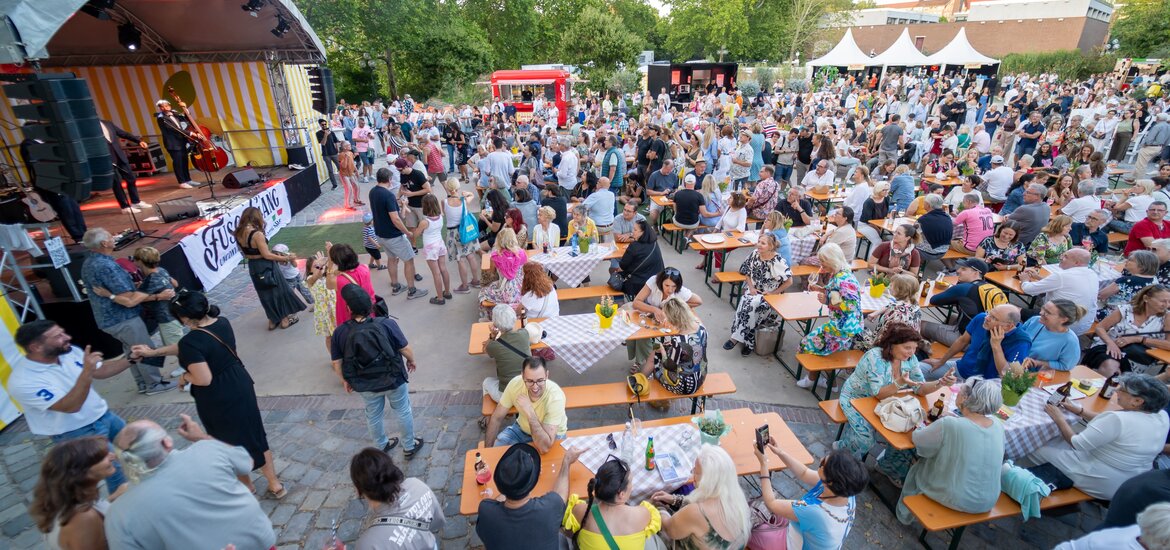 Große Menschenmenge sitzt an Biergartenbänken vor einer Bühne mit Musikern unter freiem Himmel bei La Festa Italiana Nürnberg