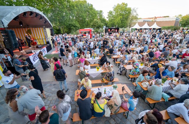 Große Menschenmenge sitzt an Biergartenbänken vor einer Bühne mit Musikern unter freiem Himmel bei La Festa Italiana Nürnberg