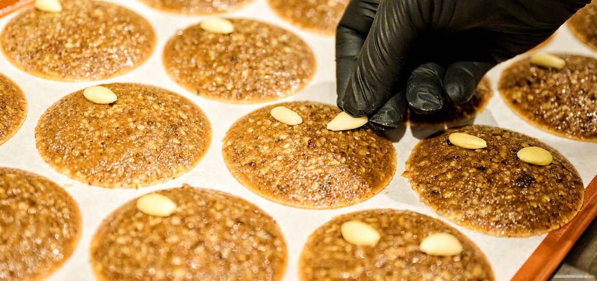 Hand legt eine Mandel auf runde Lebkuchen auf einem Backblech bei Lebkuchen-Schmidt in Nürnberg.