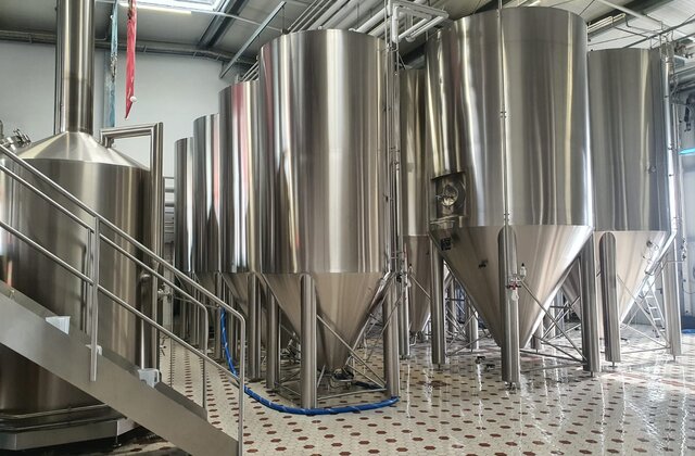 Innenansicht der Schanzenbräu Brauerei mit mehreren großen, glänzenden Edelstahltanks auf einem gefliesten Boden.