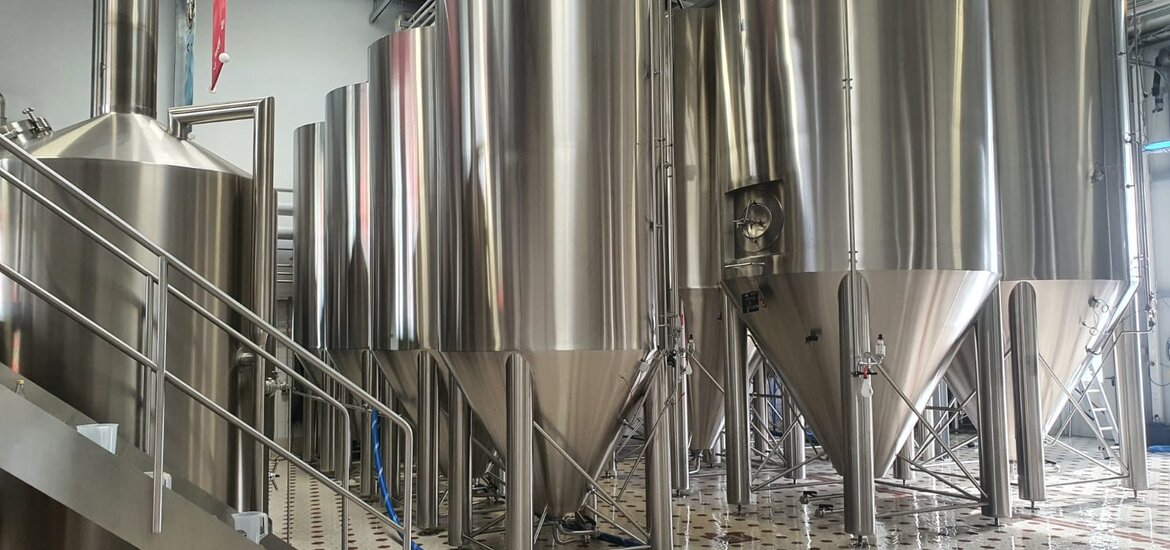 Innenansicht der Schanzenbräu Brauerei mit mehreren großen, glänzenden Edelstahltanks auf einem gefliesten Boden.