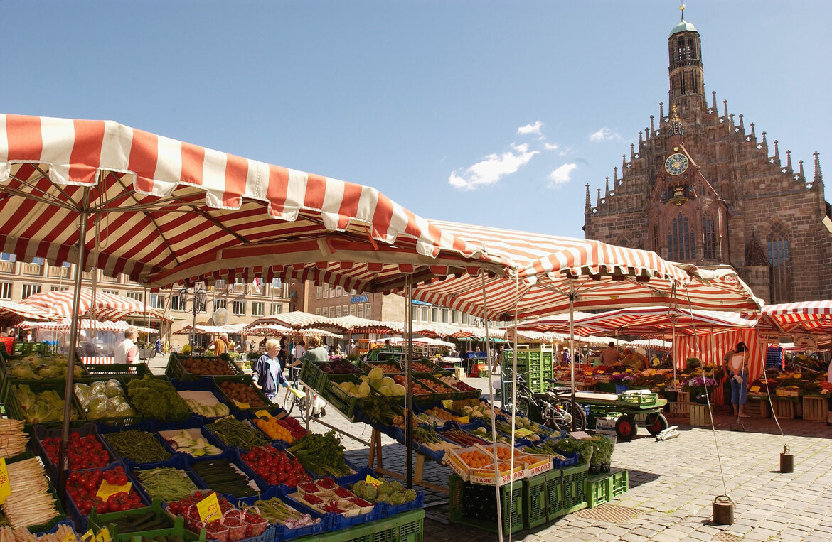 Marktstände mit rot-weiß gestreiften Planen auf dem Nürnberger Hauptmarkt vor der Frauenkirche bei sonnigem Wetter