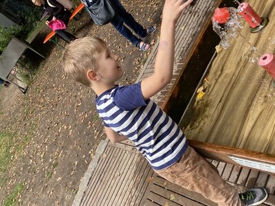 Kind mit gestreiftem T-Shirt steht an einem hölzernen Wasserspiel mit spritzenden Wasserfontänen im Erfahrungsfeld Nürnberg