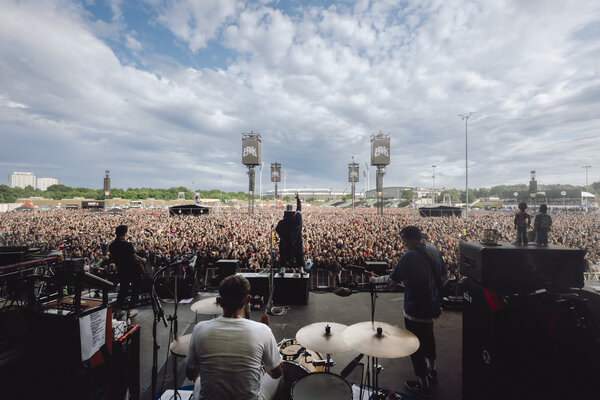 Blick von der Bühne auf eine große Menschenmenge bei Rock im Park mit Musikern und Schlagzeug im Vordergrund unter bewölktem Himmel 