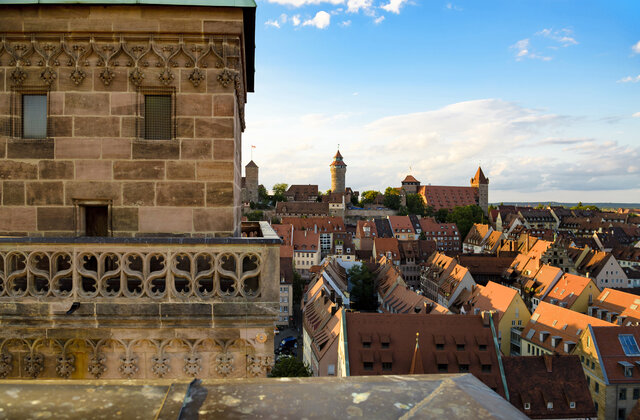 Vom detailreich verzierten Sandsteinturm der Sebalduskirche bietet sich ein weiter Blick über die rötlichen Ziegeldächer der Nürnberger Altstadt bis hin zur thronenden Kaiserburg am Horizont.