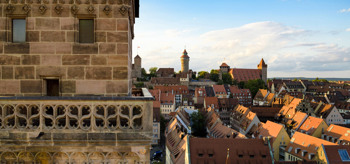 Vom detailreich verzierten Sandsteinturm der Sebalduskirche bietet sich ein weiter Blick über die rötlichen Ziegeldächer der Nürnberger Altstadt bis hin zur thronenden Kaiserburg am Horizont.