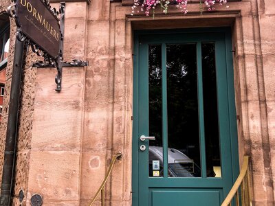 Zu sehen ist die türkise Eingangstür eines Sandstandhauses zu Dornauers Ladengeschäft