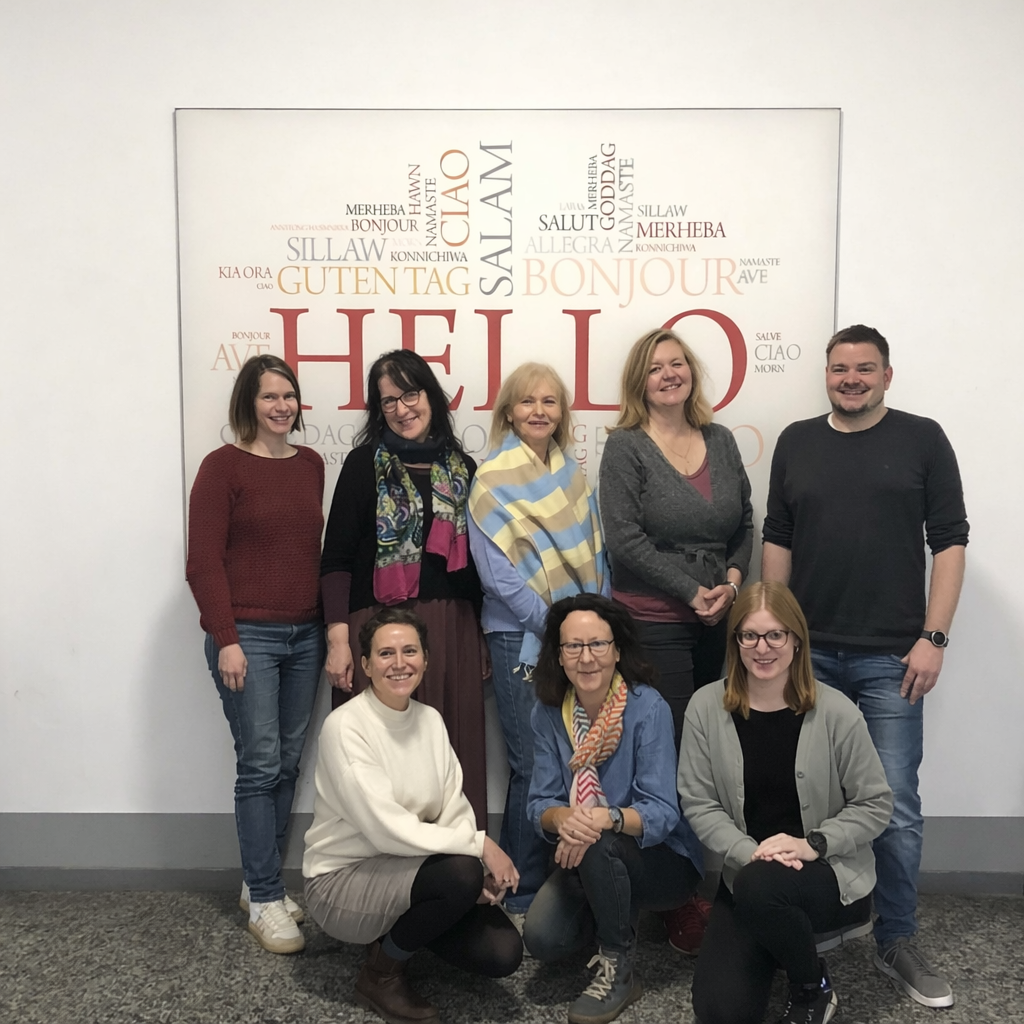 Gruppenfoto des Teams der Tourist Information Nürnberg vor einer Wand mit dem Wort "HELLO" und verschiedenen Begrüßungen in mehreren Sprachen